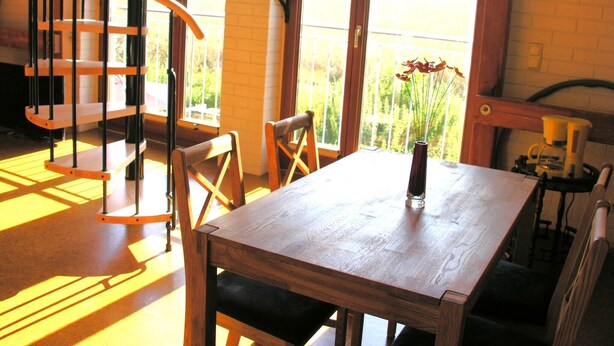 Una mesa de comedor de madera con sillas, un florero con flores, una cafetera y una escalera.