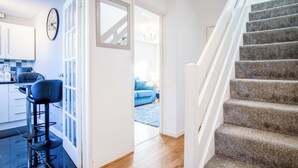 A modern kitchen with bar stools, a dining area with a blue sofa, and a staircase leading to another level. - Gellionen - 2 Bedroom House - Clydach (Swansea)