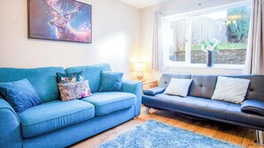 A living room with a blue sofa, a black sofa, and a painting of a deer on the wall. - Gellionen - 2 Bedroom House - Clydach (Swansea)