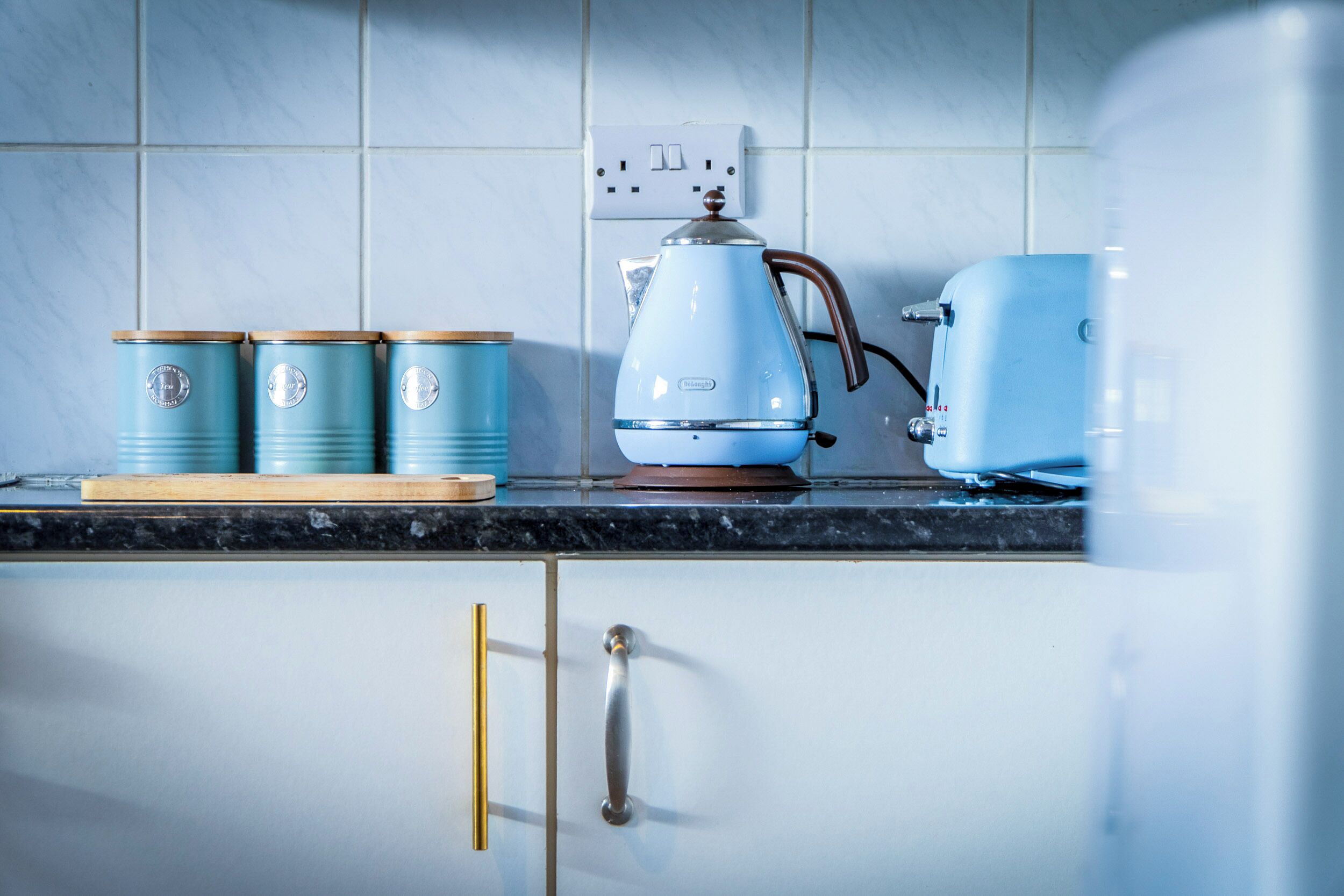 A kitchen with a blue kettle, a toaster, and three blue containers on the counter.