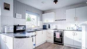 Moderni keittiö, jossa on valkoiset kaapit, sisäänrakennettu uuni, mikroaaltouuni ja kahvinkeitin.