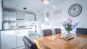Moderni keittiö, jossa on valkoiset kaapit, puinen ruokapöytä ja seinällä oleva kello.