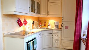 A kitchen with white cabinets, a stove, a coffee maker, and a red curtain. - Haus Achterwiek – Apartment with Private Terrace (Wolgast)