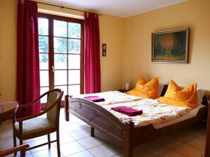 A bedroom with a bed, a chair, a window with curtains, and a painting on the wall.