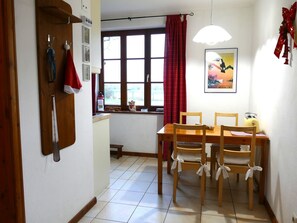 A dining area with a wooden table and chairs, a window with red curtains, a wall-mounted light fixture, and a poster on the wall.