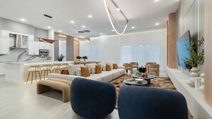 Ein modernes Wohnzimmer mit einer Couch, zwei blauen Sesseln, einem Couchtisch und einem Fernseher an der Wand.