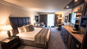 Ein Hotelzimmer mit einem großen Bett, einem Schreibtisch mit Lampe, einer Couch, einem kleinen Tisch und einer Küchenzeile.