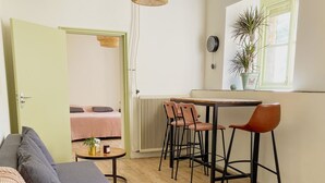 Een gezellige woonkamer met een bank, een klein rond tafeltje, en een keukenhoek met een eettafel en stoelen.