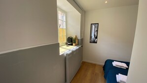 A narrow hallway with a radiator, a window, a mirror, and a bed with folded towels.