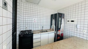 A kitchen with white tiled walls, a gas stove, a sink, and a refrigerator with a beverage advertisement. - Charming Studio Near the Airport Gln0805 (Recife)