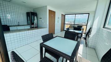 Una cocina moderna con baldosas blancas, una encimera con refrigerador, y un comedor con sillas de mimbre y una mesa de vidrio.