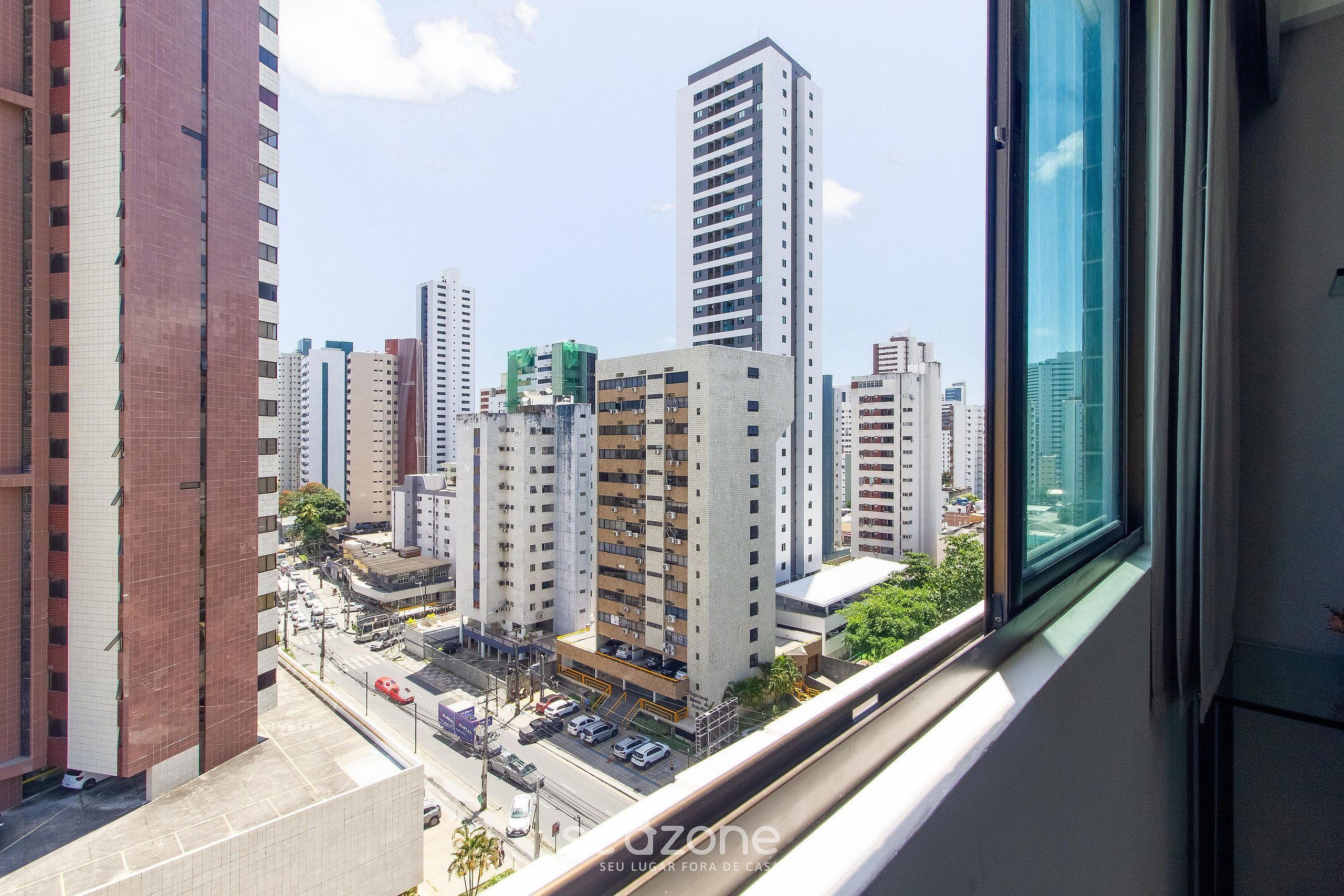 Un edificio de gran altura con varios pisos, un estacionamiento al frente y vistas de otros edificios a lo lejos.