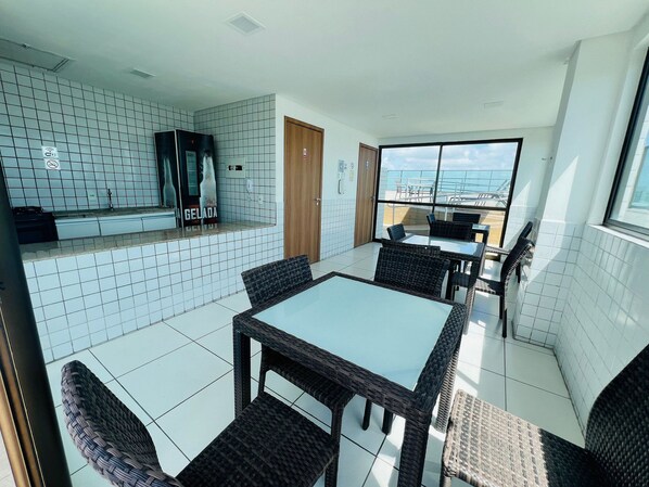 Une cuisine moderne avec des carreaux blancs, un comptoir avec un réfrigérateur, et un coin repas avec des chaises en osier et une table en verre.