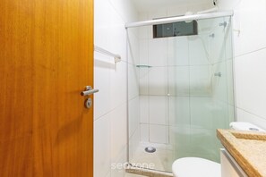 A bathroom with a glass shower enclosure, a wooden door, and a white toilet. - Charming Studio Near the Airport Gln0805 (Recife)