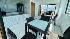 A modern kitchen with white tiles, a counter with a refrigerator, and a dining area with wicker chairs and a glass table. - Charming Studio Near the Airport Gln0805 (Recife)