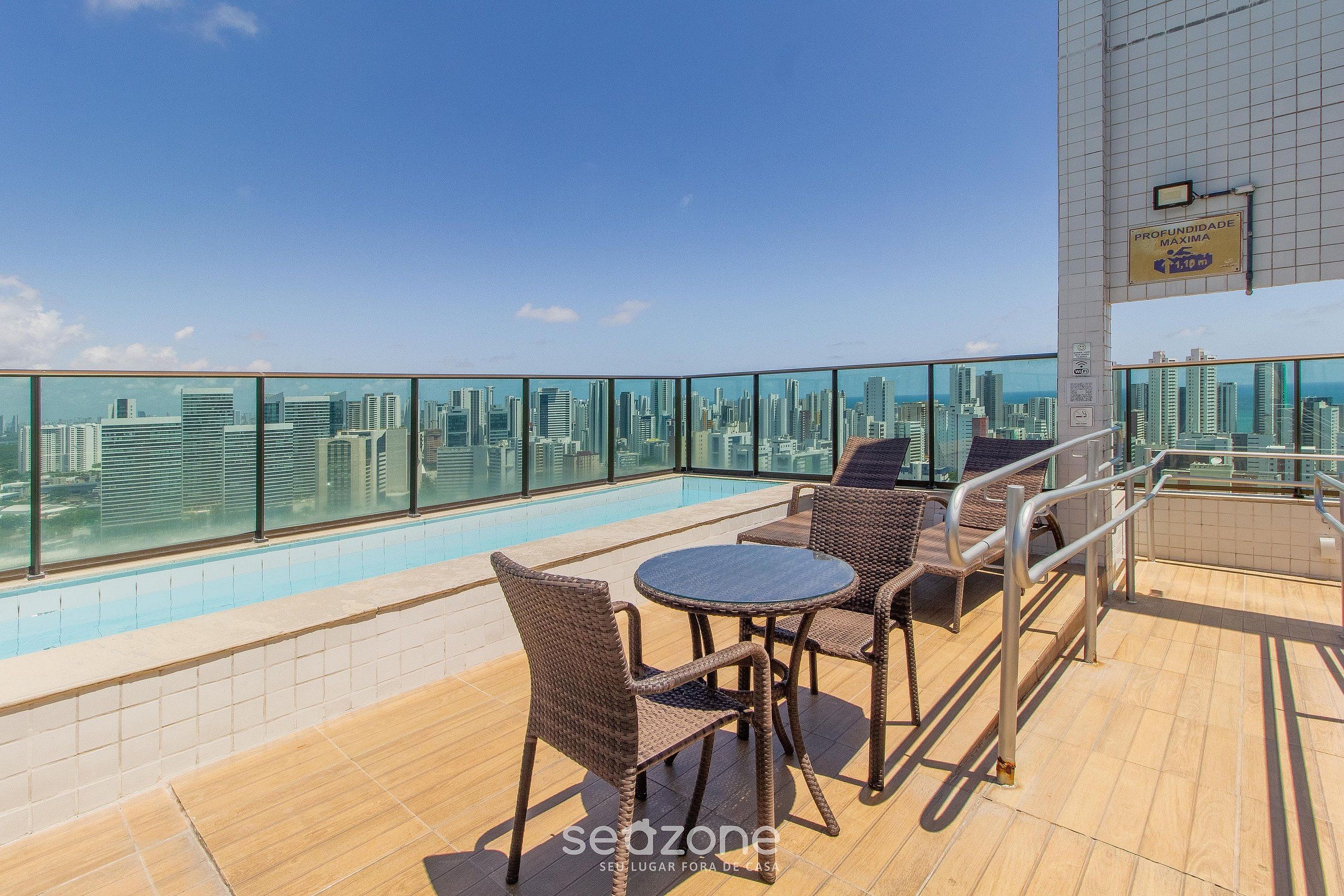 Zona de piscina en la azotea con vista a la ciudad, amueblada con sillas de mimbre y una pequeña mesa redonda.