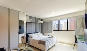 A modern hotel room with a bed, a desk, and a view of tall buildings. - Charming Studio Near the Airport Gln0805 (Recife)