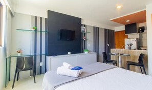 A modern hotel room with a bed, a desk, a chair, a TV, and a kitchenette.