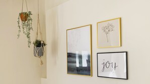 Een muur met drie ingelijste kunstwerken en twee hangplanten.