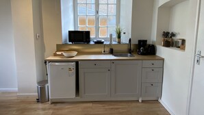 Een kleine keuken met een raam, een magnetron, een spoelbak en een compacte koelkast.