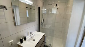 Een moderne badkamer met een wit wastafelmeubel, spiegel en een douchecabine met glazen wanden.