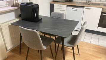 A kitchen with a dark wooden table, two grey chairs, a coffee maker, a microwave, and a dishwasher.