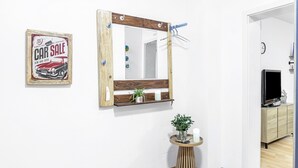 Una habitación con un espejo de marco de madera, una mesita con una planta en maceta y un cartel de venta de coches antiguos en la pared.