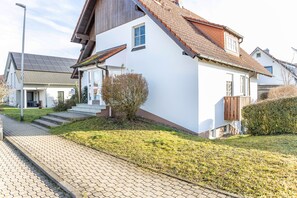 Una casa moderna con techo inclinado, un pequeño porche delantero y un sendero pavimentado que conduce a la entrada.