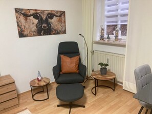 Una sala de estar moderna con un sillón negro, una mesita redonda con una planta, una mesita de madera y una gran obra de arte de un toro.