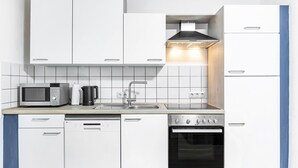 Una cocina compacta con armarios blancos, microondas, cafetera, lavavajillas y horno.