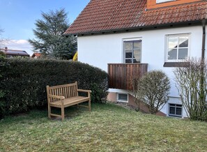 Una casa con banco de madera, fachada blanca y tejado de tejas rojas.