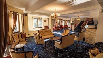 A hotel lobby with a patterned carpet, seating area with armchairs and a sofa, a chandelier, and a staircase leading to another level.