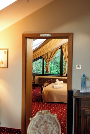 A hotel room with a bed, a wooden nightstand, a mirror, and a window with curtains. - Classic Inn Hotel (Brasov)