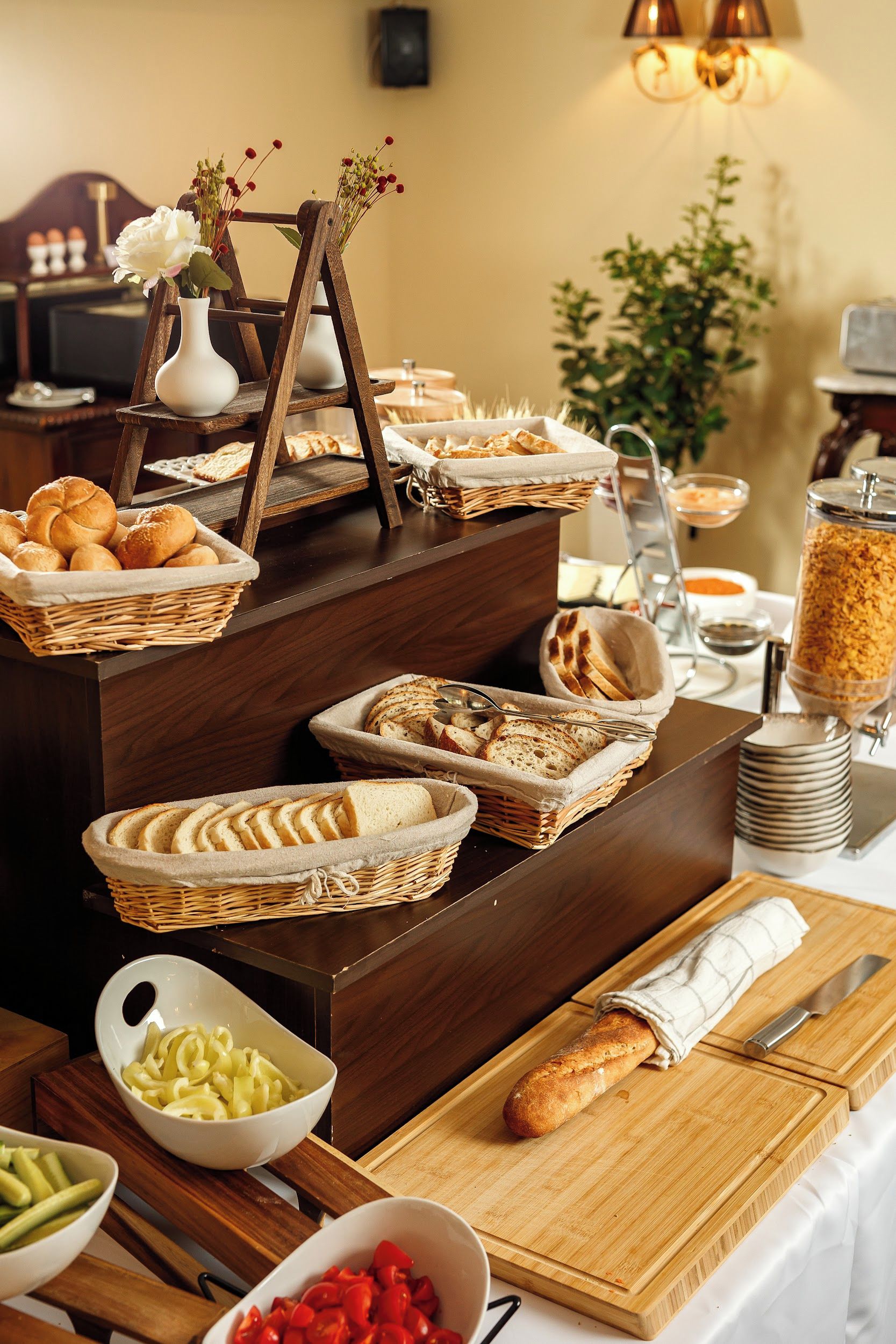A buffet setup with various food items, including bread, vegetables, and a decorative vase with flowers.