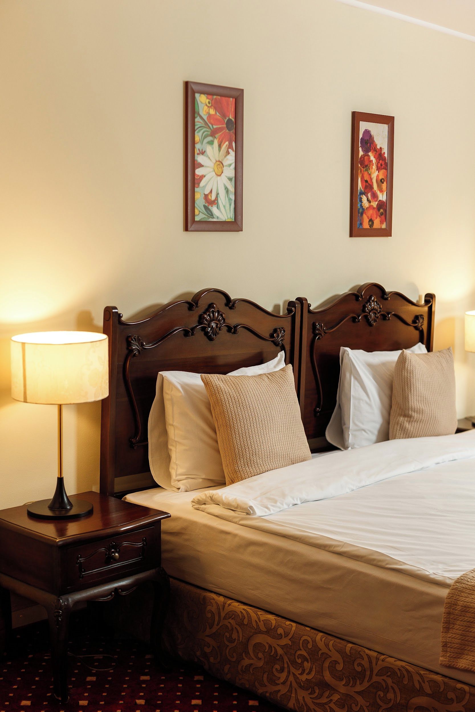 A hotel room with a large bed, two nightstands, a lamp, and two floral paintings on the wall.