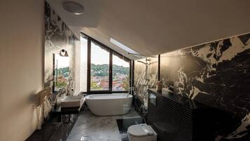 A modern bathroom with a bathtub, a large window, and a view of a cityscape.