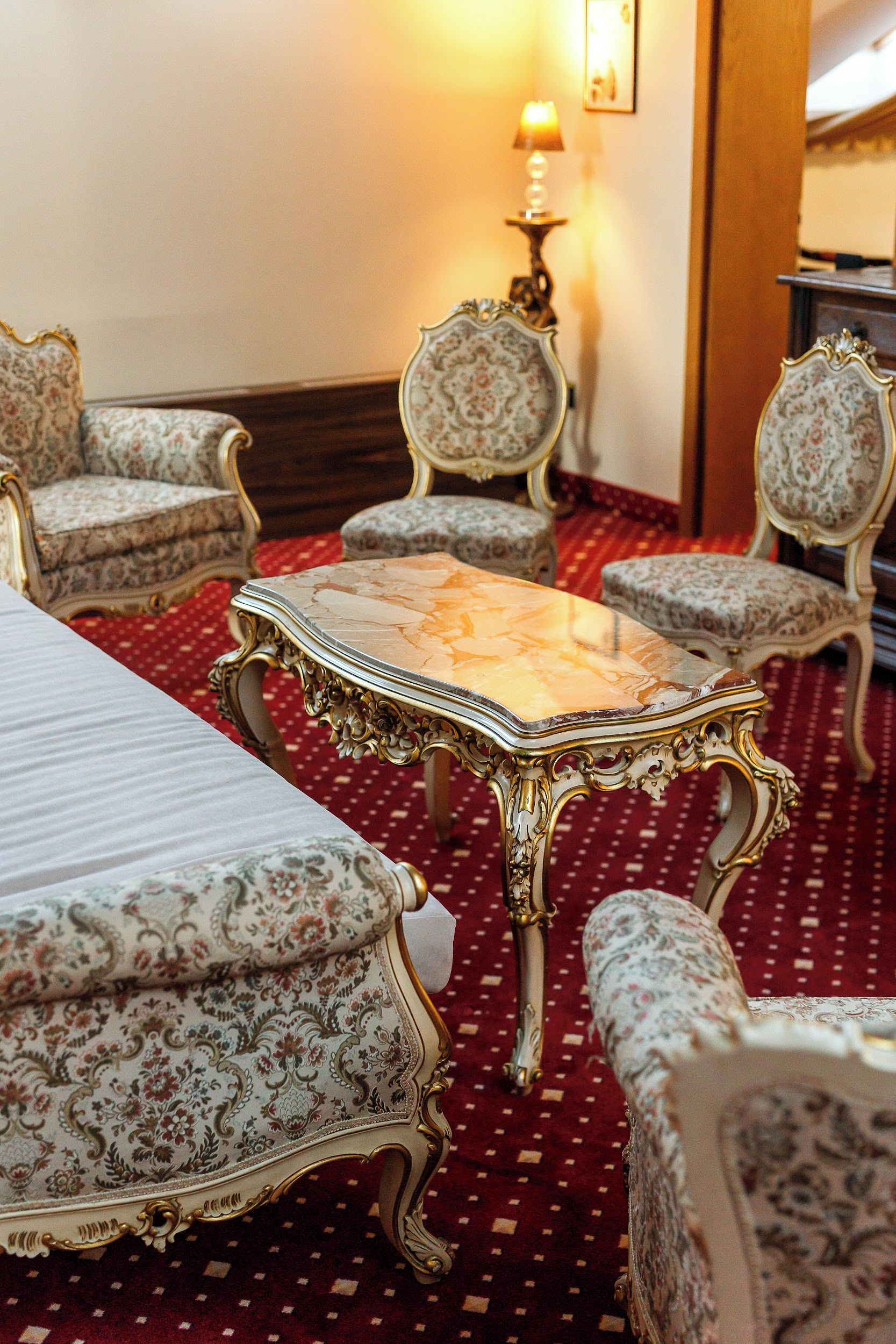 Quarto de hotel com cama, mesa e quatro cadeiras estofadas com estampas florais.