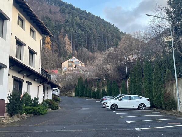 A street with parked cars, a building with a sign, and a mountain in the background. - Classic Inn Hotel (Brasov)