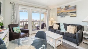A living room with a glass table, a sofa, and a chair. There is a balcony with a view of the sea. - Ocean View Top Floor - 2 Pools - Hot Tub - GYM - Tennis (Galveston)