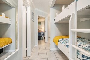 Un couloir étroit, avec des lits superposés de chaque côté, qui mène à une pièce comprenant un lit et un bureau.
