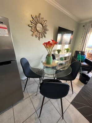 Une cuisine compacte comprenant un réfrigérateur, une table à manger en verre avec des chaises, un miroir décoratif et un téléviseur.