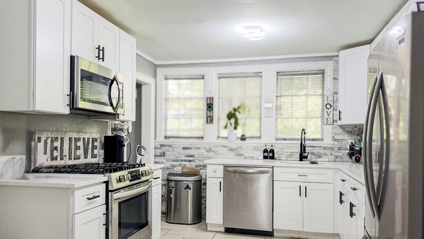 A modern kitchen with white cabinets, stainless steel appliances, and a tiled backsplash. - Cozy Winter Escape - Hot Tub, Game Room, Fireplace, Sleeps 6 (Waterbury)
