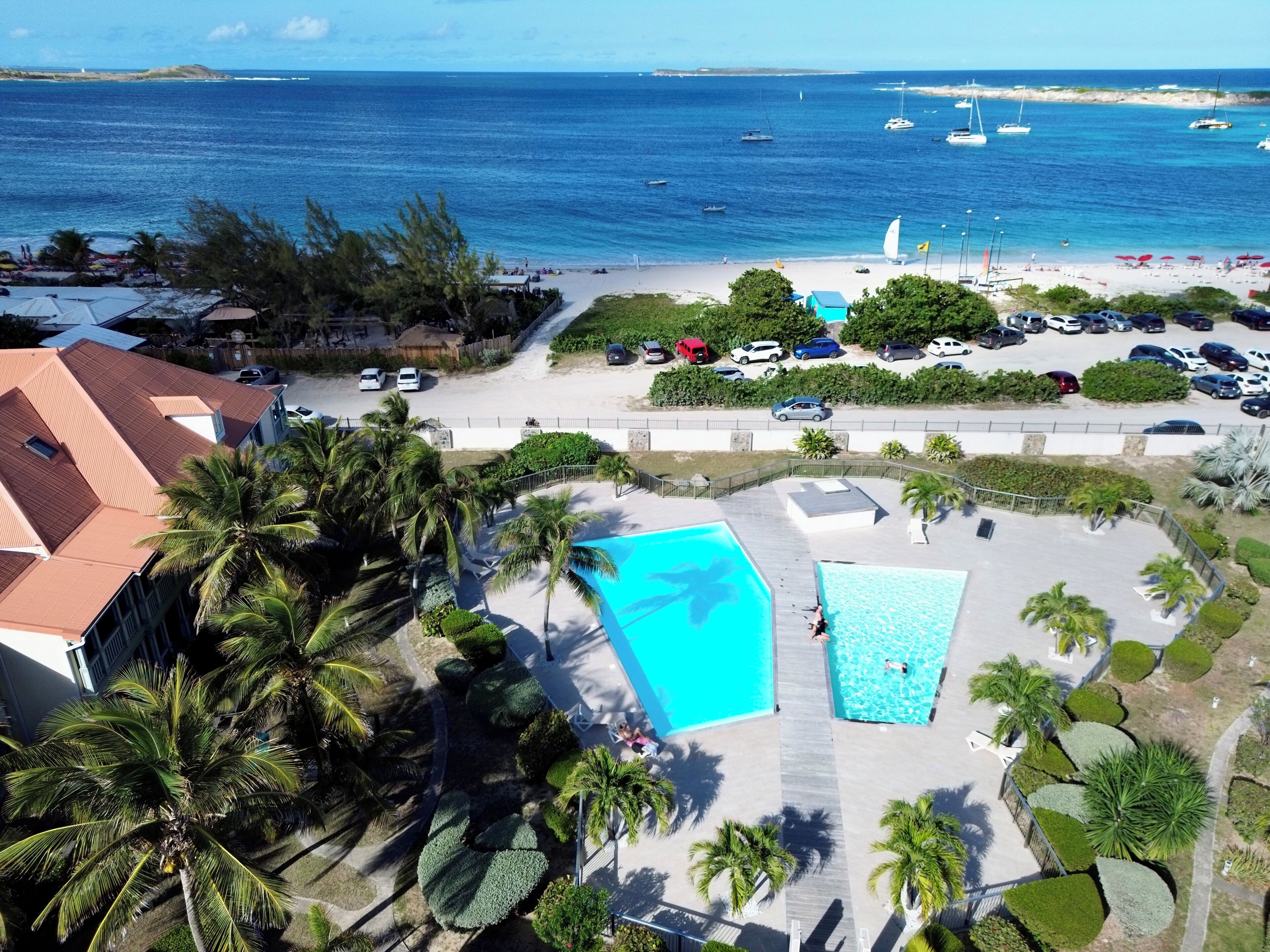A resort with a large swimming pool, a beach with boats, and a parking area.