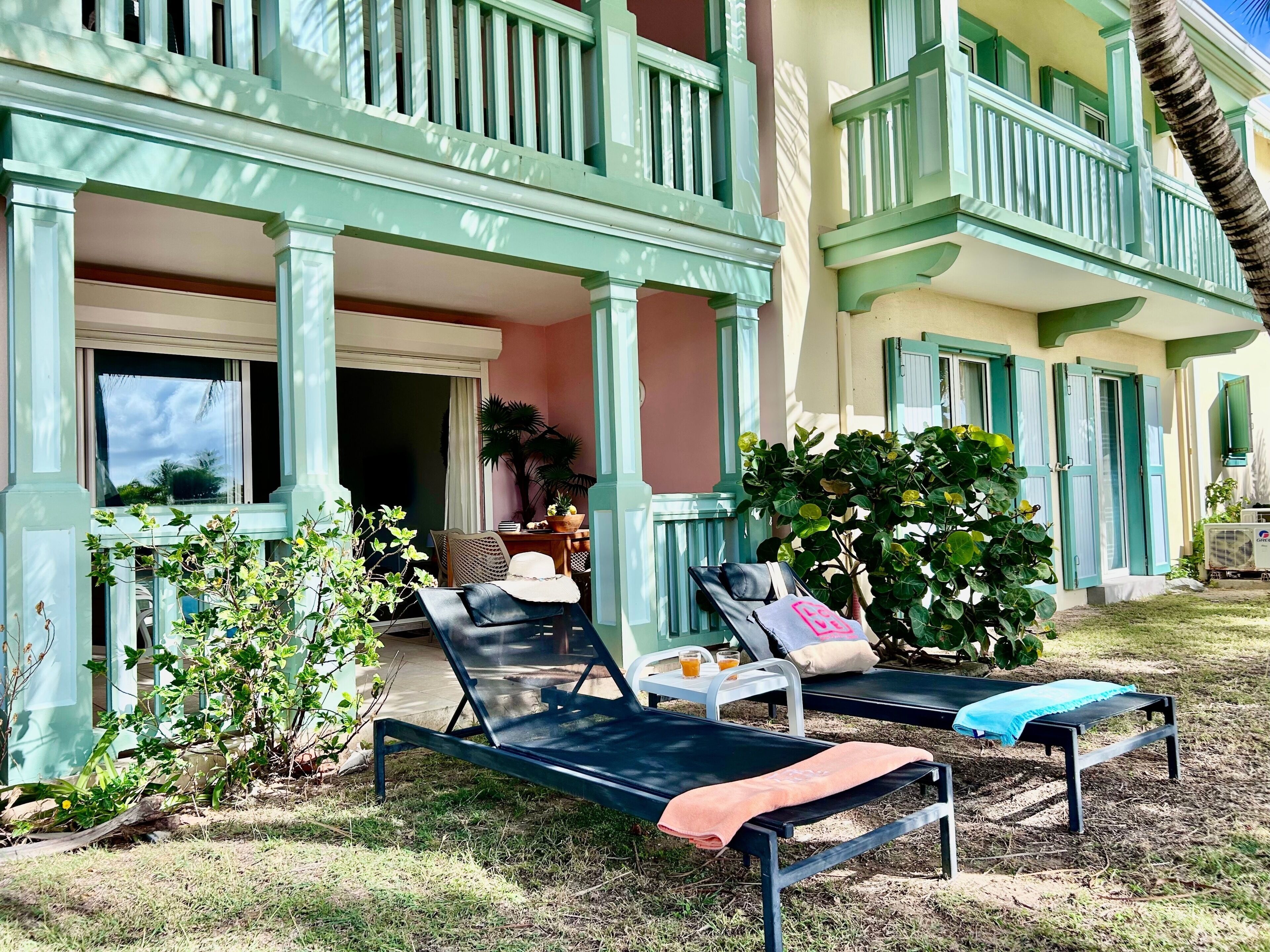 Un bâtiment à deux étages doté d’un balcon, d’un espace extérieur aménagé pour s’asseoir et d’une petite table avec une boisson.