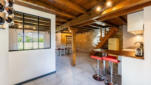 A kitchen with wooden beams, a stone wall, a window, and a bar area. - La Ferme – Château Le Noble: Charm, Comfort, and Nature Among the Vineyards (Saint-Germain-du-Puch)