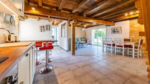 A kitchen with wooden beams, a bar area, and a dining area with stone walls and a view of greenery. - La Ferme – Château Le Noble: Charm, Comfort, and Nature Among the Vineyards (Saint-Germain-du-Puch)