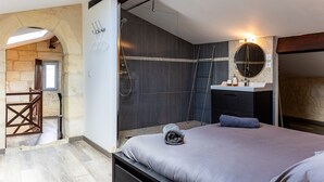 Un dormitorio con cama, un baño con ducha, tocador y un espejo grande.