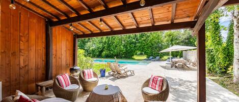 Un patio al aire libre con mobiliario de mimbre, piscina y techo de madera.