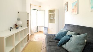 Ett modernt vardagsrum med en grå soffa, blå kuddar, en vit hylla och en liten lampa.
