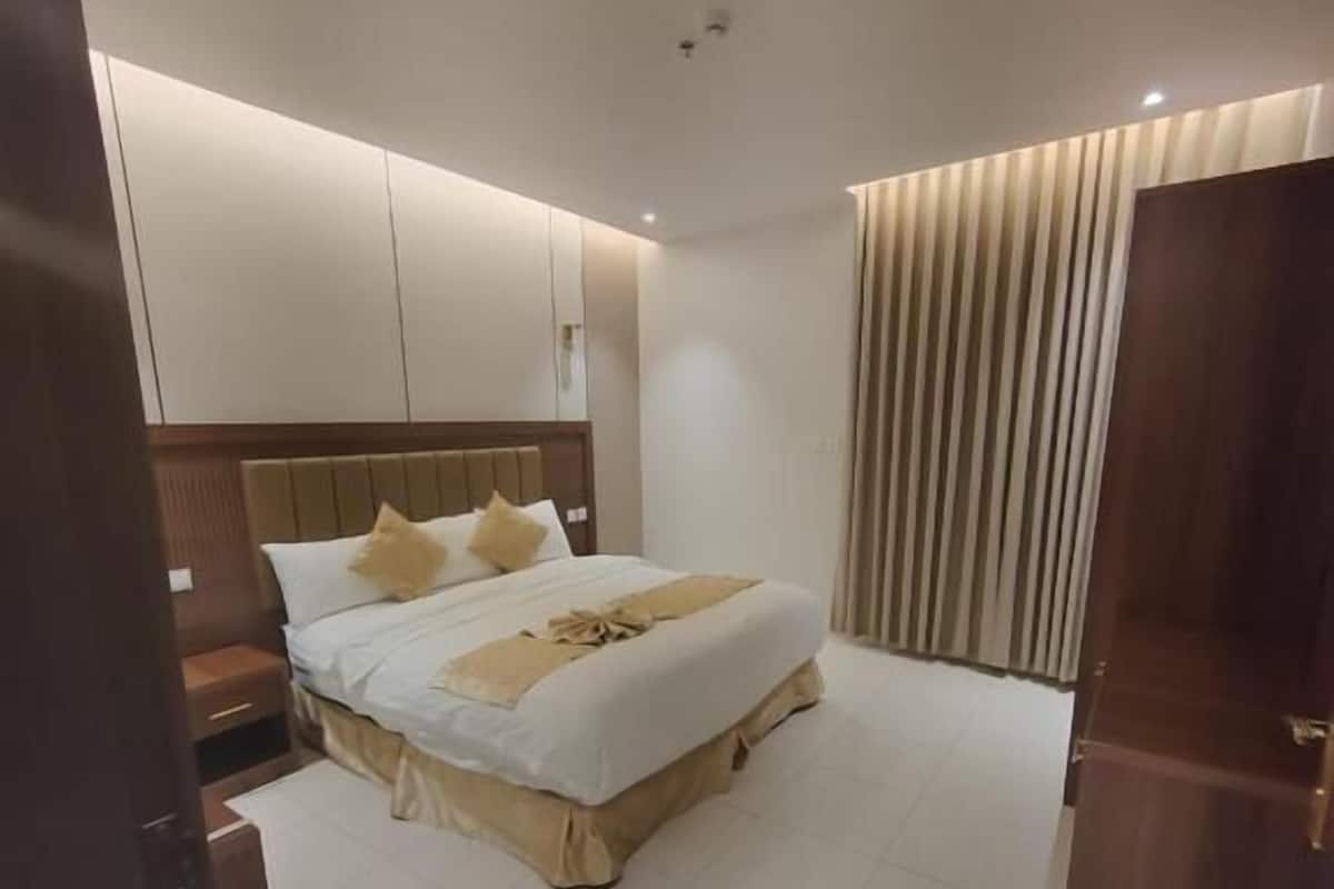 A hotel room with a large bed, a nightstand, a wooden headboard, and a curtain on the window.